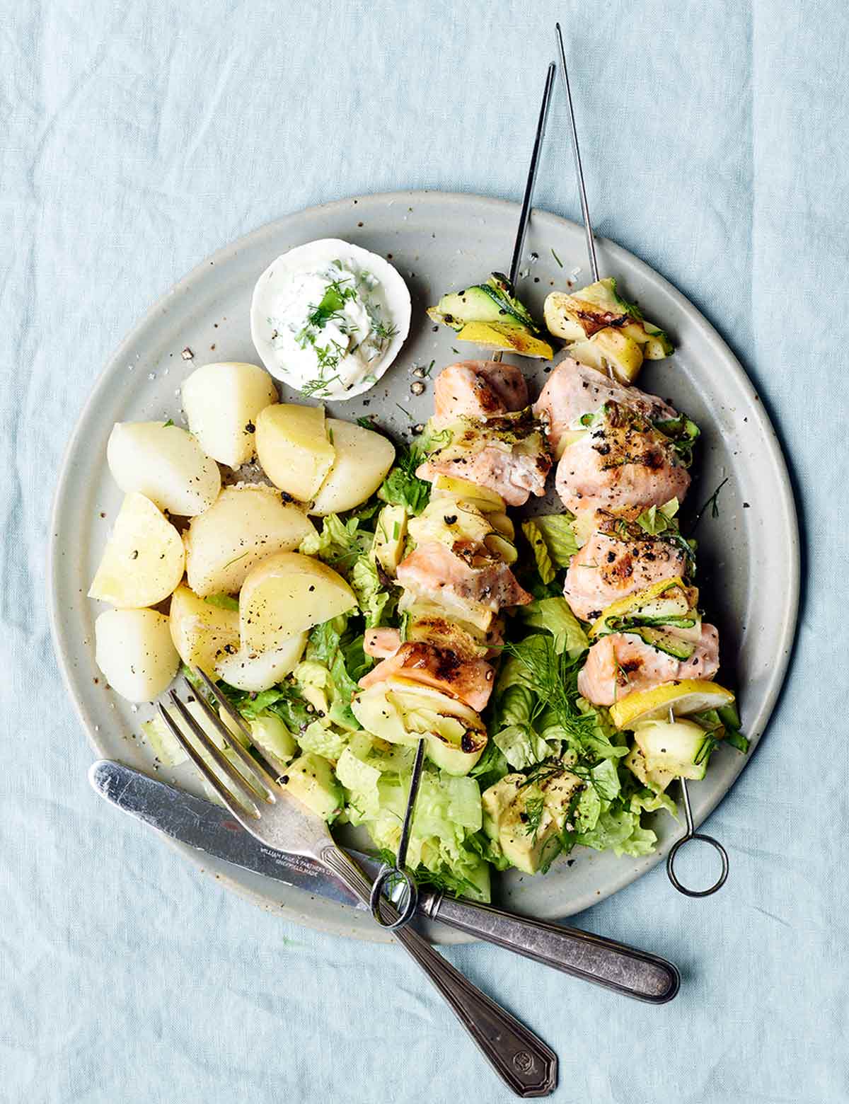 A plate with two grilled salmon and zucchini skewers with potatoes on the side