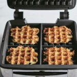 Four of Ina Garten's waffle iron hash browns in a waffle iron with the lid open.
