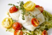 A piece of oven-roasted halibut with cherry tomatoes and thyme on a bed of cooked cabbage.