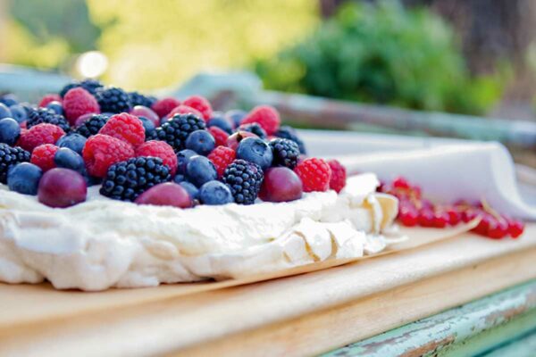 A pavlova with fresh berries on a wooden table outside.