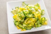 A tangle of sautéed summer squash ribbons on a square white plate.