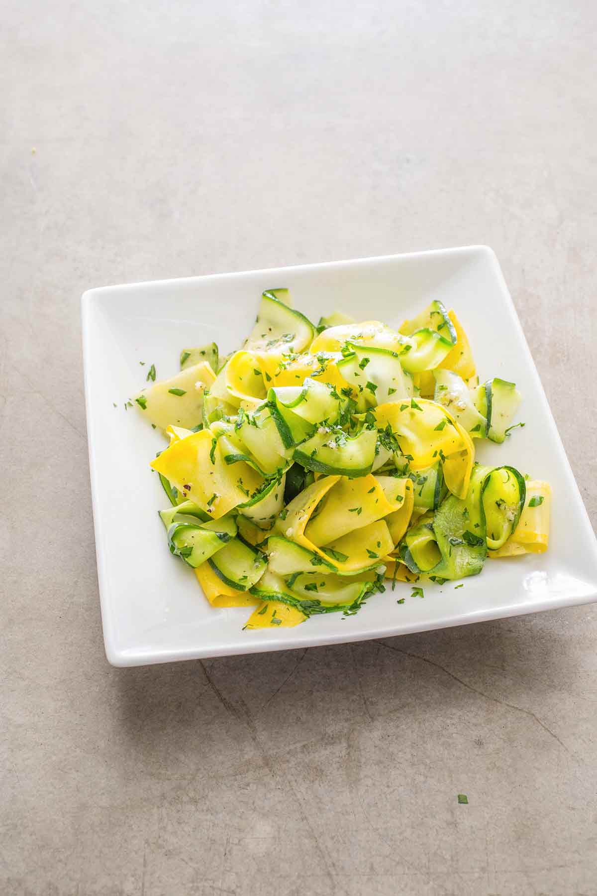 A tangle of sautéed summer squash ribbons on a square white plate.