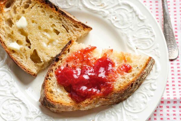 Two pieces of buttered toast, one with strawberry jam, on a white plate.