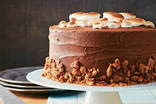 A s'mores cake, topped with toasted marshmallows and graham cracker crumbles on a cake stand.