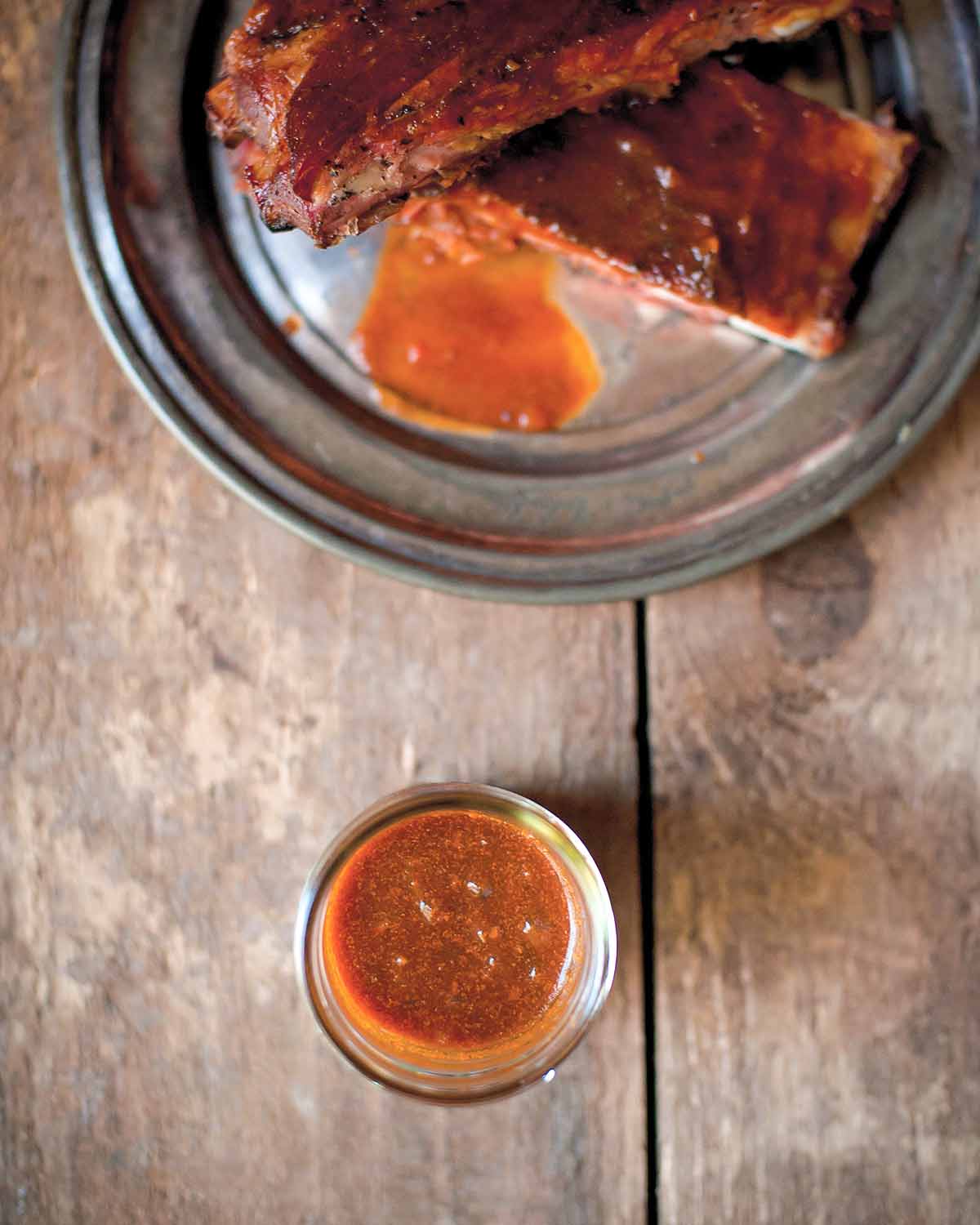 A platter of ribs covered with Texas-style barbecue sauce, and a glass of extra sauce on the side.