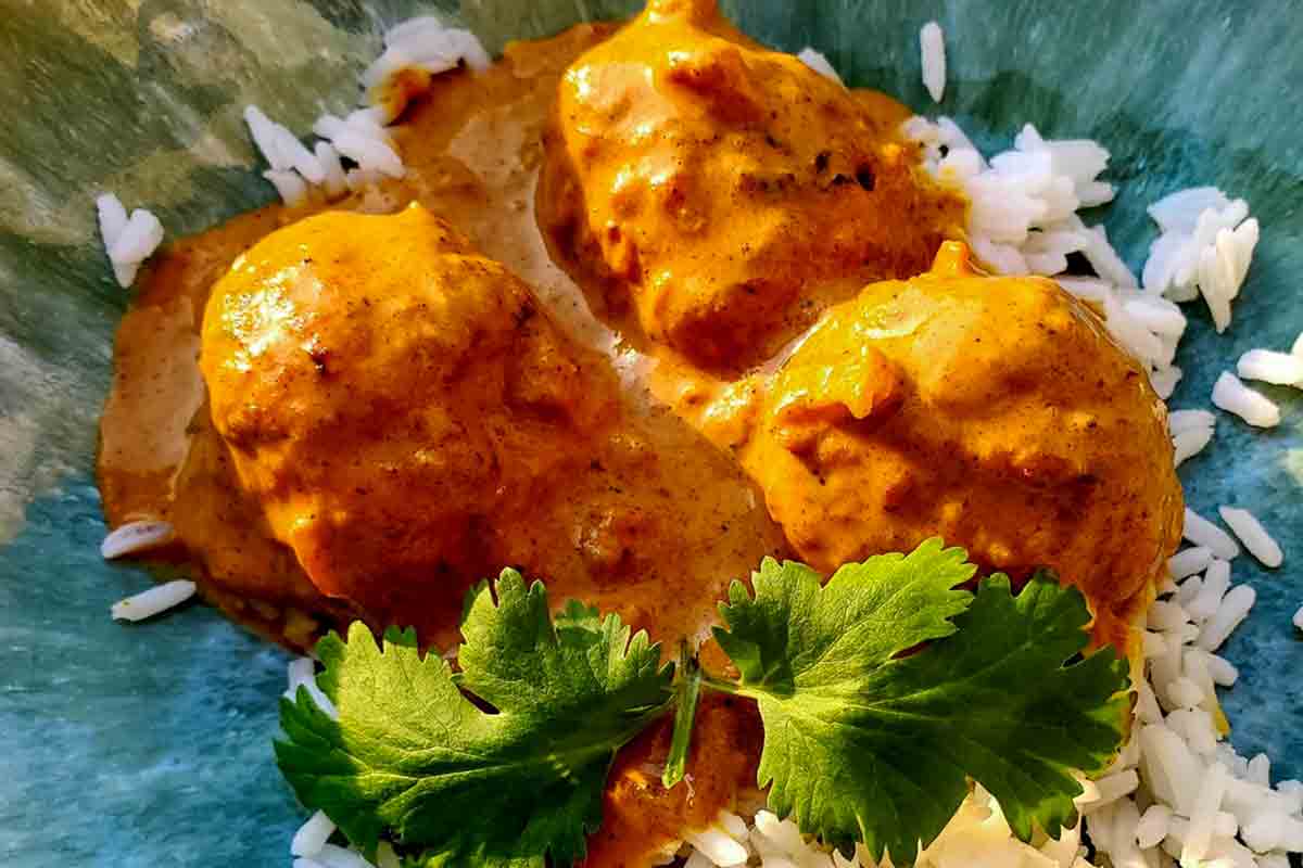 A plate topped with white rice and three chicken tikka masala meatballs, garnished with cilantro.