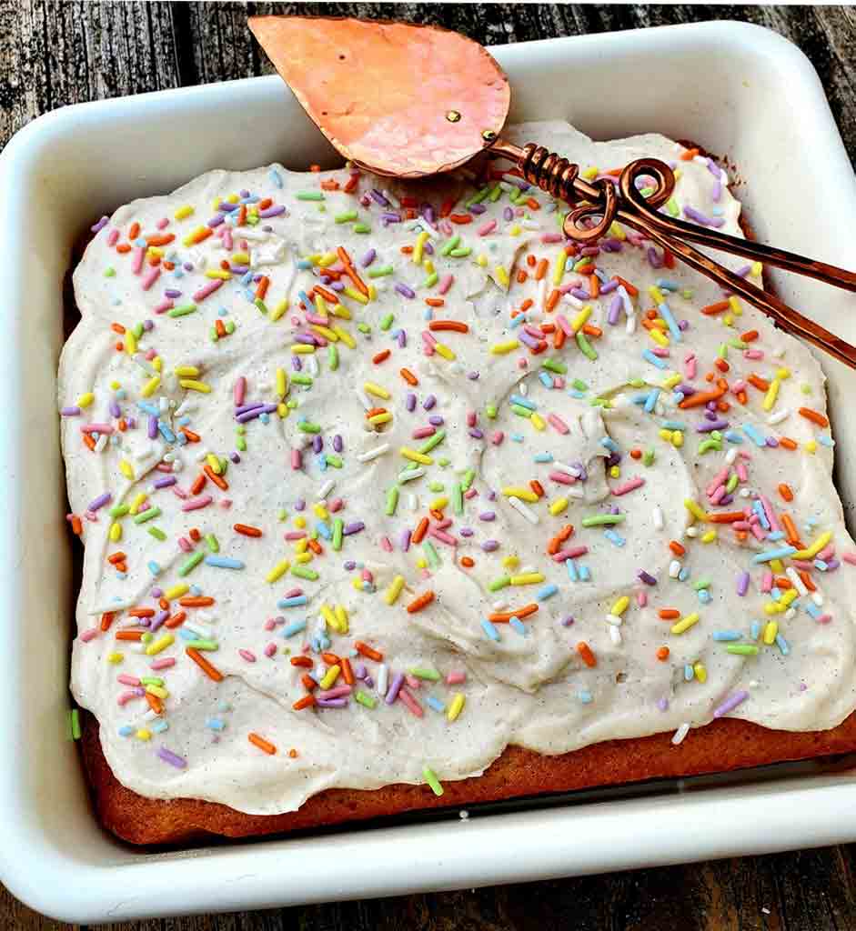 A square vanilla buttermilk cake in a white baking dish, frosted and decorated with sprinkles.