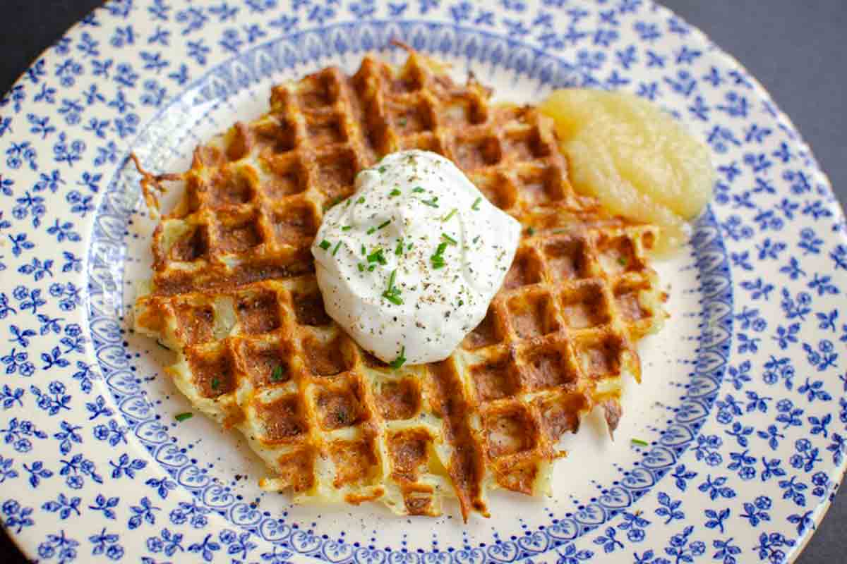 One of Ina Garten's waffle iron hash browns on a plate, topped with cream and a dollop of apple sauce on the side.