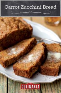 A loaf of carrot zucchini bread with candied ginger on a white platter with three slices cut from it and buttered.