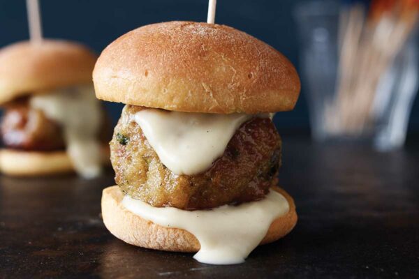 A chicken meatball on a slider bun with a toothpick skewered through it.
