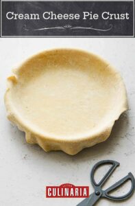 Empty pie crust in a pie plate, with kitchen shears next to it.