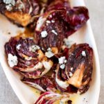 A white platter, piled with quartered grilled radicchio topped with crumbled Gorgonzola cheese.