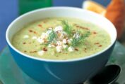 A blue bowl filled with a pale green cream soup, topped with paprika, feta, and fresh dill fronds.