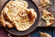 Three cheese and chile naan bread, drizzled with butter, in a metal dish on a wooden table, beside pieces of naan.