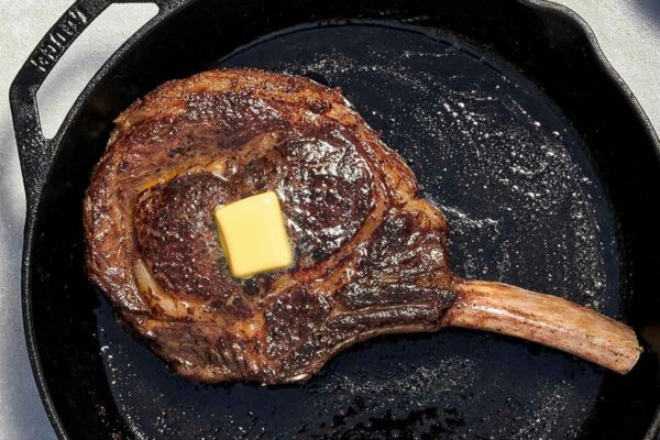 A large rib eye steak with a pat of butter on top, in a cast iron pan.