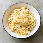 A big white bowl filled with spaghetti, chunks of artichokes, hazelnuts, flecks of chile pepper flakes, and Parmesan cheese.