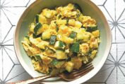 A green bowl filled with scrambled eggs and green pieces of zucchini on a tile tabletop, with a fork.