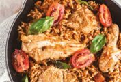 A cast-iron skillet with chicken, orzo, tomatoes, and garnished with basil.