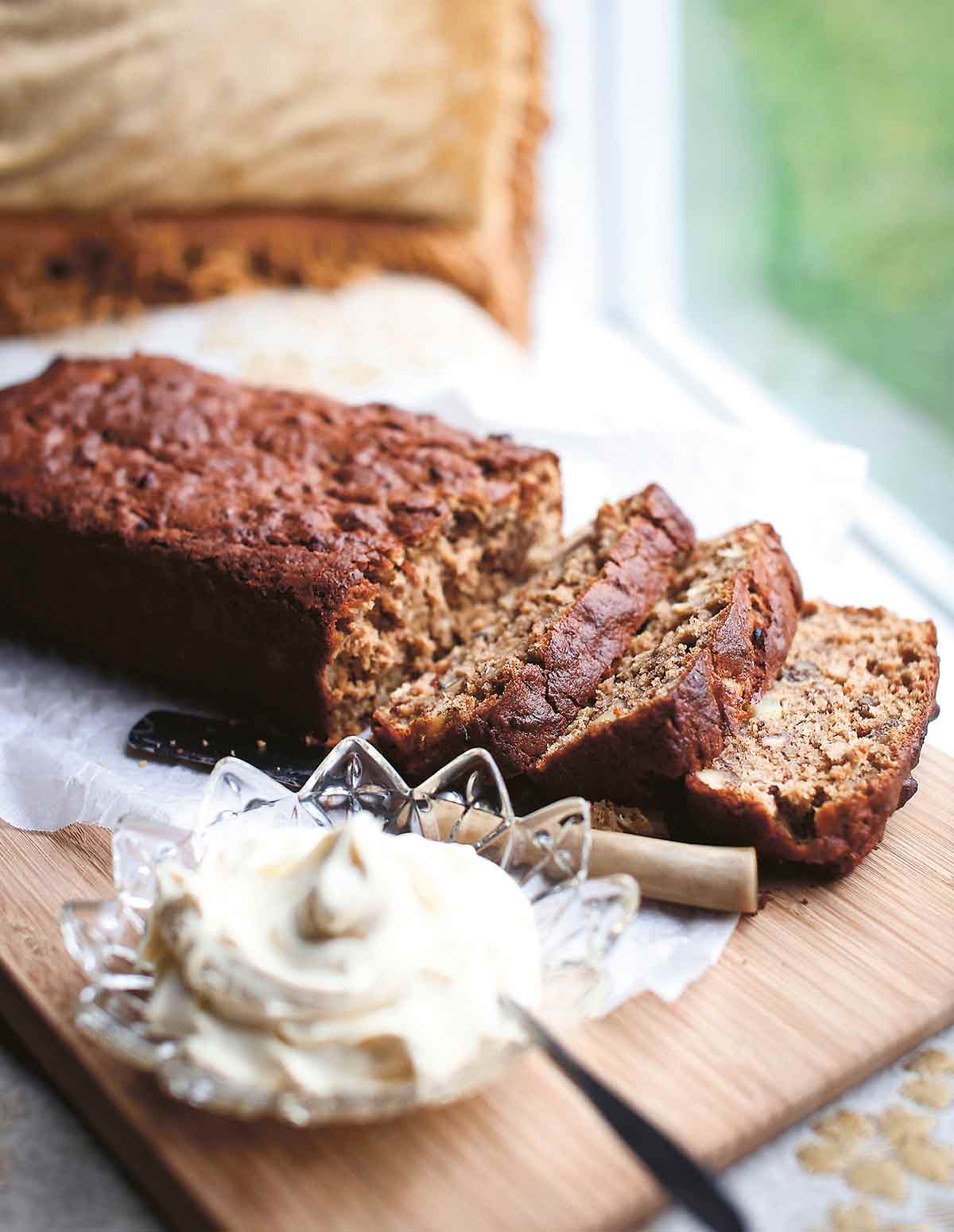 A sliced loaf of hummingbird loaf cake, beside a glass dish of butter and a butter knife.