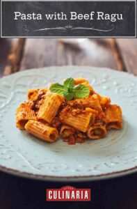 A light blue plate with a serving of rigatoni pasta covered with beef ragu, garnished with green herbs.