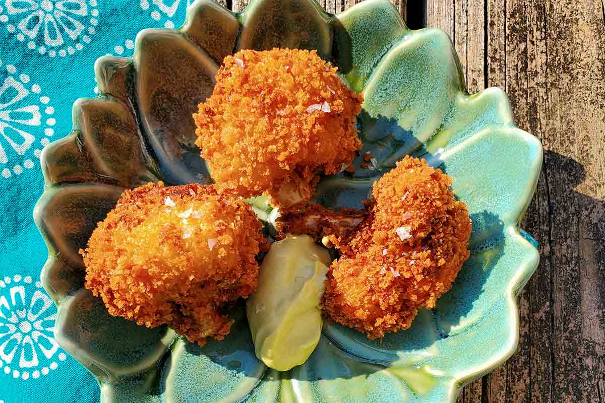 A small lotus shaped plate with 3 deep-fried, breaded cauliflower bites and a dollop of mayo dip, all sprinkled with sea salt.