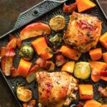 A sheet pan filled with roasted chicken thighs, apples, bacon, Brussels sprouts, and sweet potatoes.