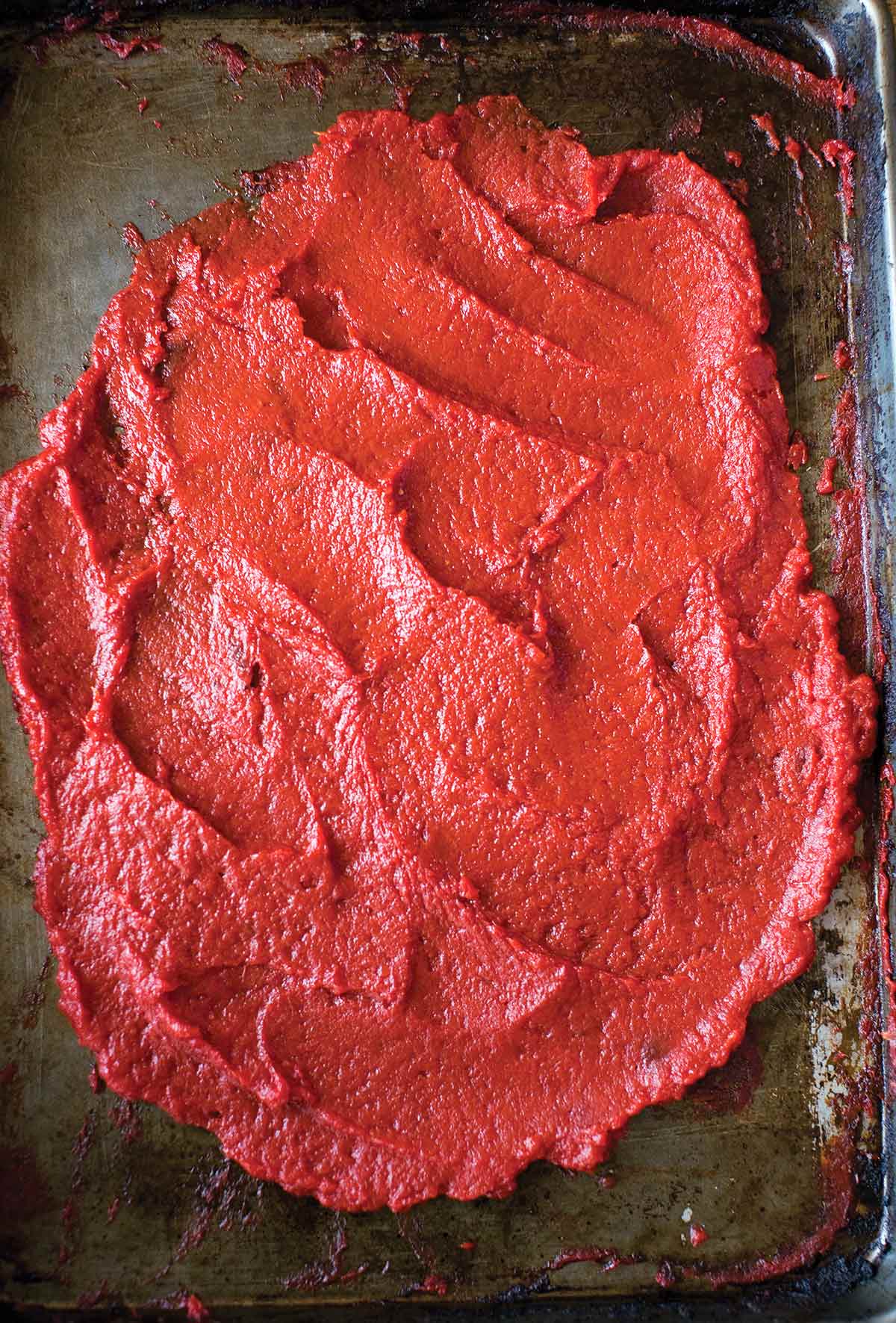 A metal sheet pan, covered with spread out tomato paste.