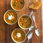 . Each bowl is filled with tomato soup with chickpeas and spinach and topped with yogurt.