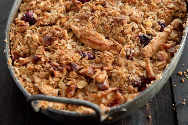 A metal oval baking dish filled with apple cranberry crisp.