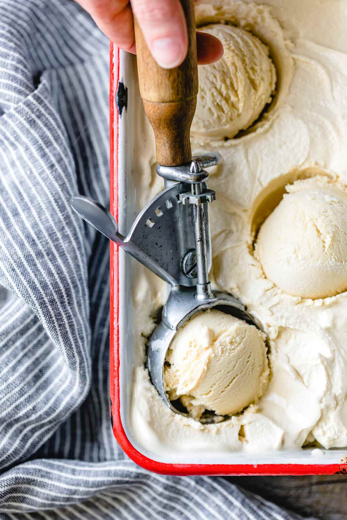 Armagnac ice cream in a metal tin, with 3 scoops and an ice cream scoop.