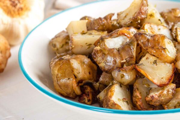 Roasted Jerusalem artichokes in a white bowl with a fork and napkin in the background.