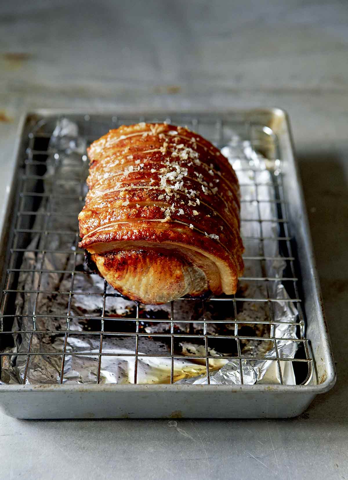 A pork loin roast, tied and seasoned with salt and pepper, on a foil-lined sheet pan with a wire rack.