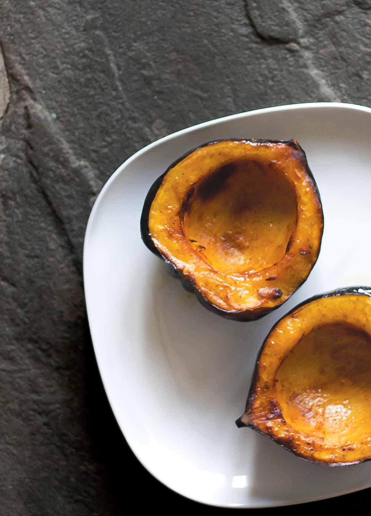 2 halves of an acorn squash on a white plate, scooped out and lightly charred.