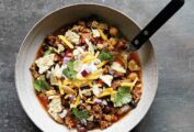A pottery bowl of slow-cooker beef chili from Skinnytaste, topped with tortilla chips, cilantro, red onions, and cheese.
