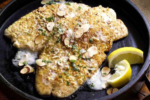 Almond flounder meunière in a wooden serving dish topped with sliced almonds and lemon wedges on the side.
