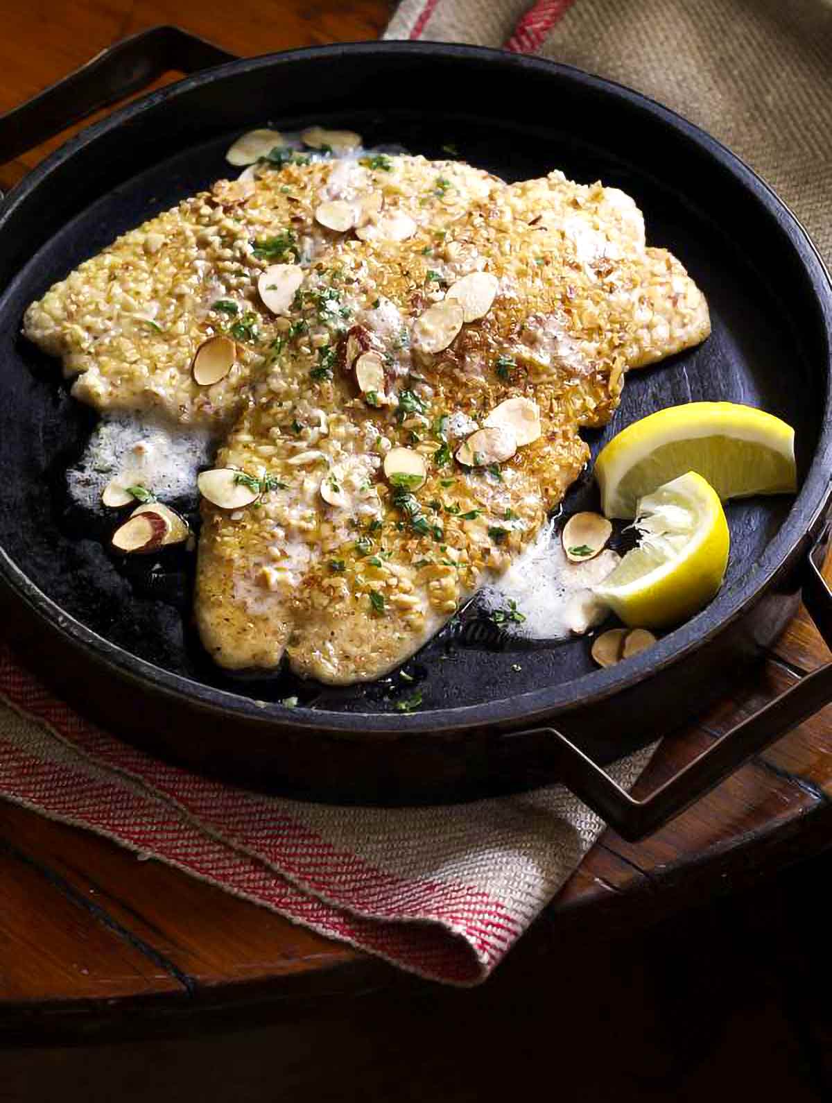 Almond flounder meunière by Dorie Greenspan in a wooden serving dish topped with sliced almonds and lemon wedges on the side.