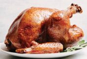 Dry brine turkey on a large white platter, garnished with fresh sage leaves.