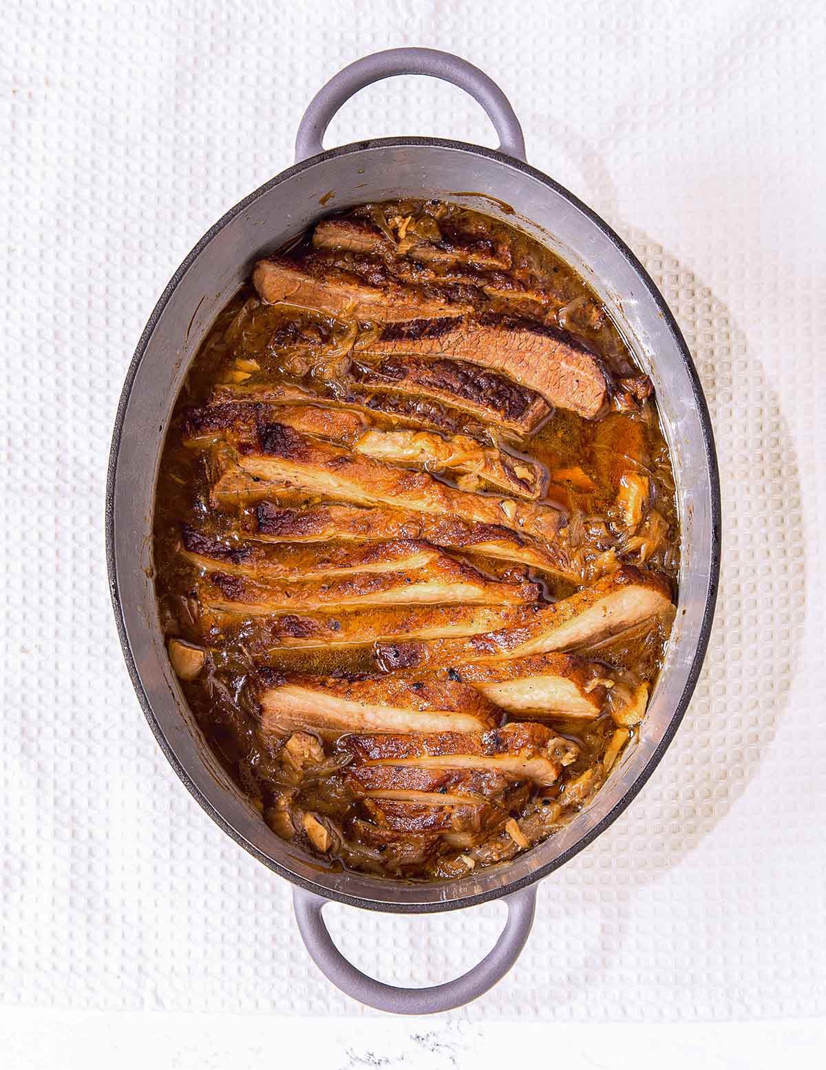 French onion brisket in an oval enamel casserole dish on a white background.