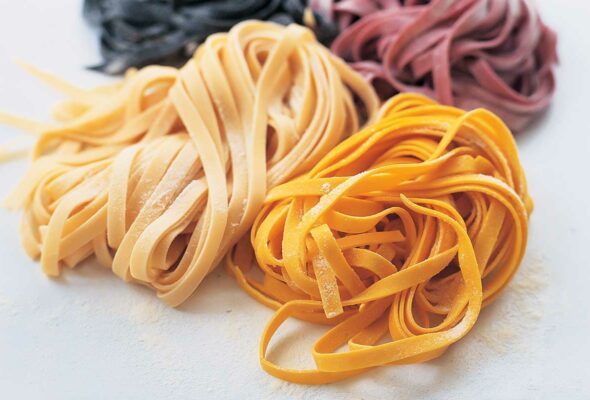 Homemade pasta dough in 4 colors, plain, squid ink, beet, and saffron on a white background.
