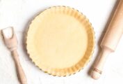 A pie crust in a fluted pie tine beside a flour scoop and a rolling pin.