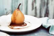 A poached pear with warm coffee sauce on a plate with a scoop of vanilla ice cream and a spoon.