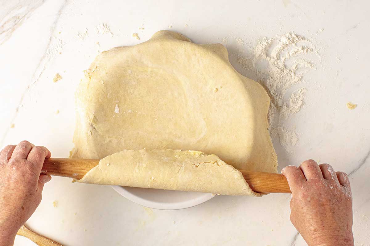A person transferring a rolled out pie crust to a plate.