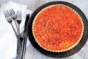 Carrot crostata on a large black plate, with a white napkin and cutlery on a wood table.