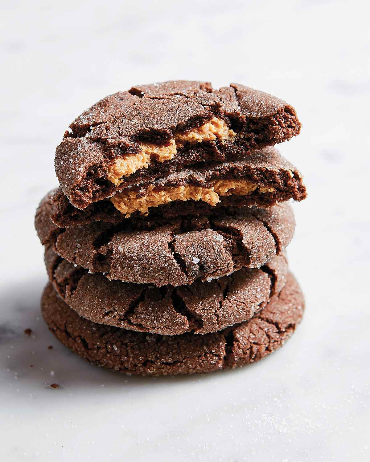 Chocolate peanut butter cookies in a stack, the top one broken in half, on a white background.