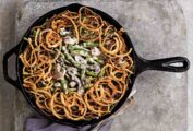 A classic green bean casserole with mushrooms and topped with fried onion rings in a cast-iron skillet.