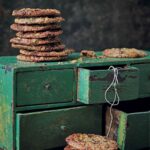 Clove cinnamon and chocolate cookies stacked up on a green cupboard with twine and another stack of cookies in front.