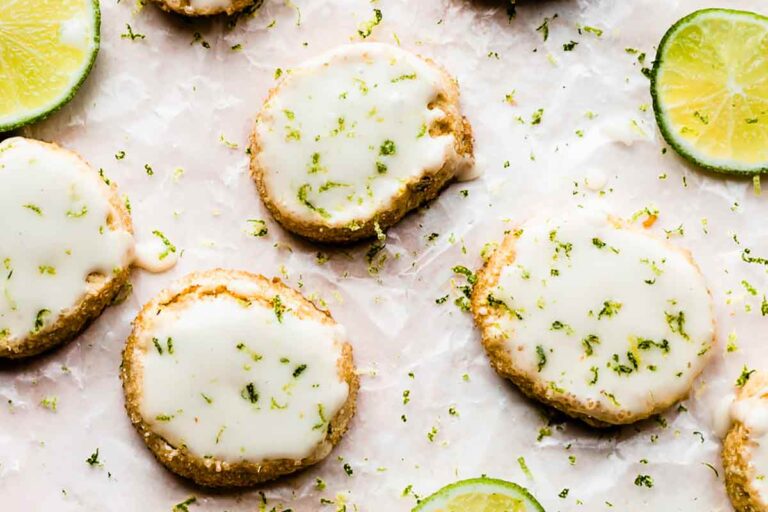 Key lime slice and bake cookies garnished with lime zest beside slices of lime, all on a sheet of parchment paper.