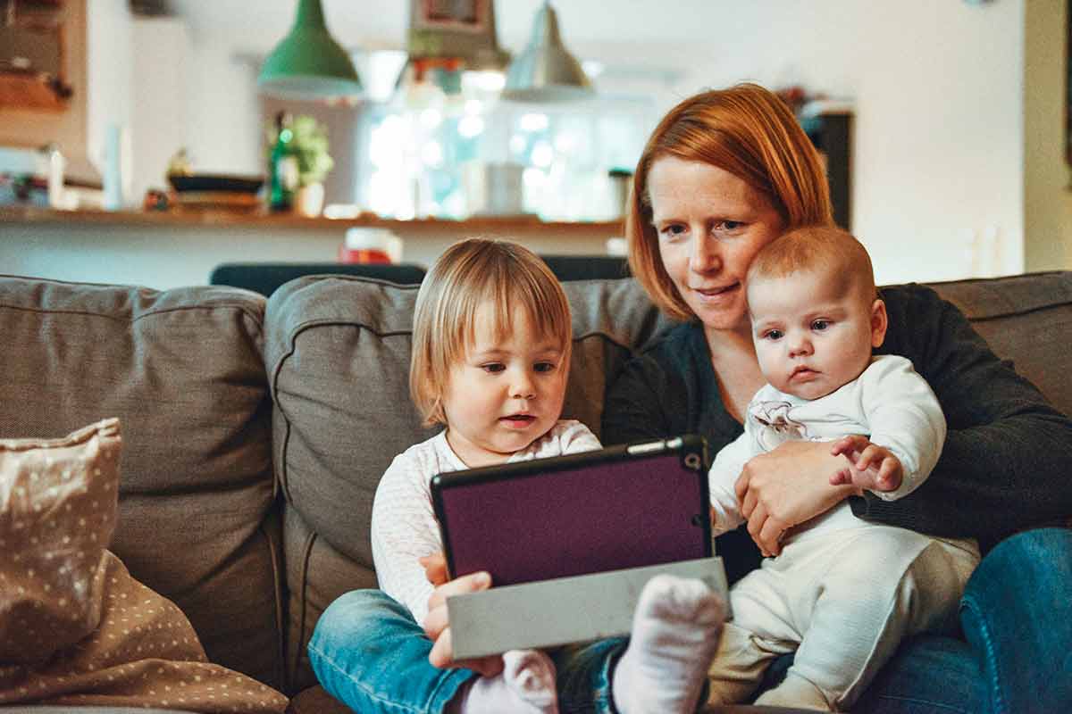 A woman holding a baby and sitting next to a child while watching something on a tablet.