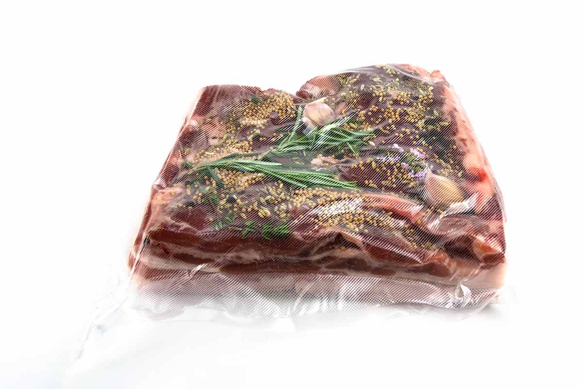 A piece of meat with rosemary sprigs and mustard seeds vacuum sealed in a bag.