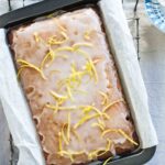 Spiced gingerbread with lemon glaze garnished with lemon zest strips, in a parchment-lined cake pan.